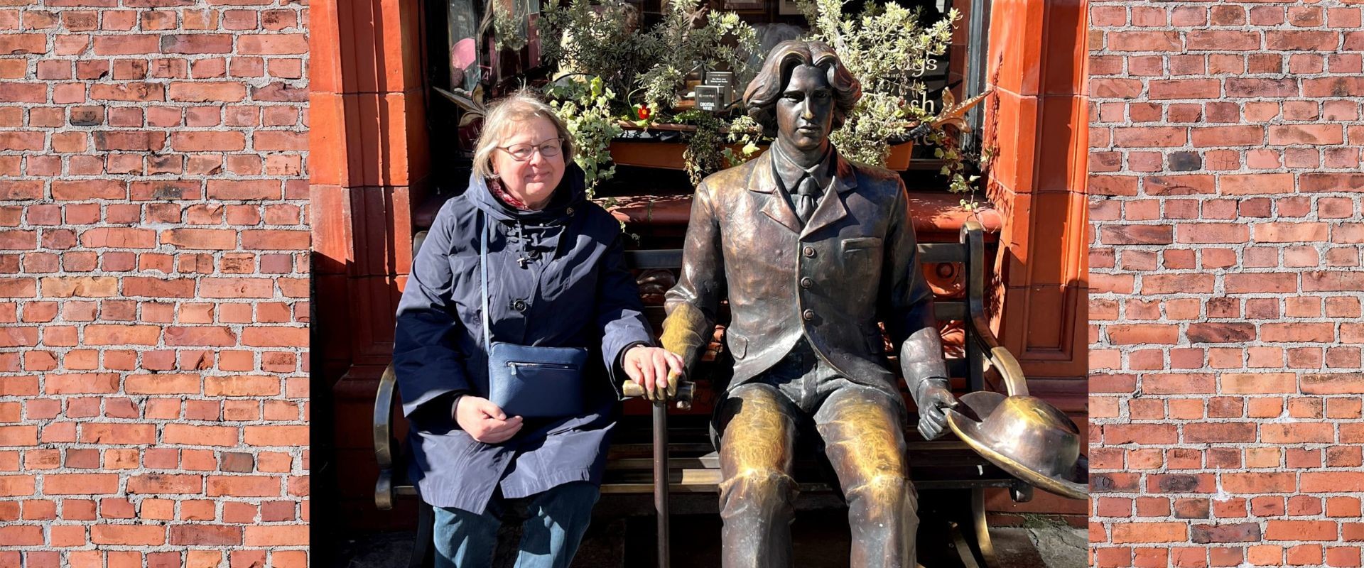 Kirjastotoimenjohtaja Maarit Järveläinen istuu penkillä Oscar Wilde -patsaan vieressä ja hymyilee.