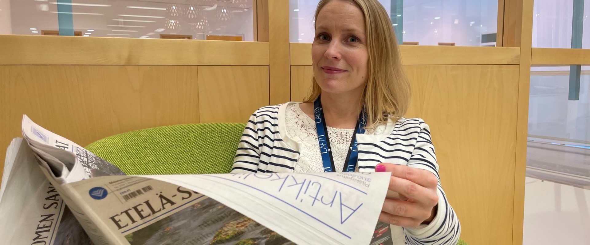 Kirjaston hanketyöntekijä Kaisa Halme lukee paperista Etelä-Suomen Sanomat -lehteä ja katsoo hymyillen kameraan.