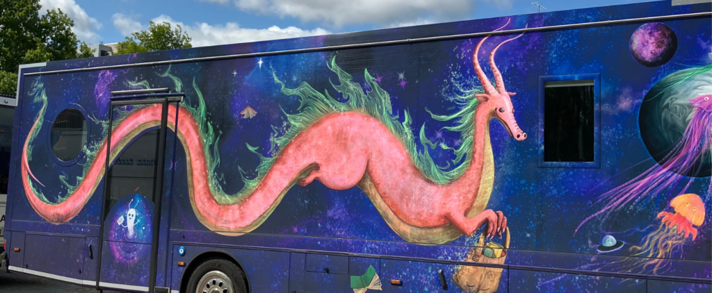 Tampereen Kosmos-kirjastoauton kyljen kuvituksena vaalenpunainen lohikäärmehahmo violetilla pohjalla.