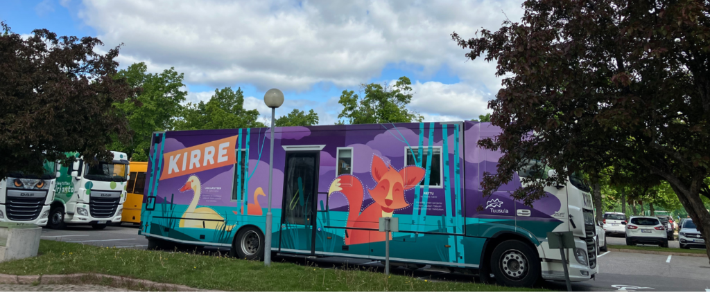 Tuusulan kirjastoauto kirre kuvattuna sivulta päin. Sini-violetti-oranssin kyljen kuvituksena kettu, järvi, jossa ui joutsenia, ja isolla teksti KIRRE.