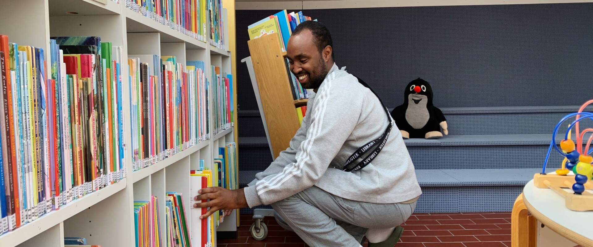 Jibril Mohamud hyllyttää kyykyssä lasten kuvakirjoja.