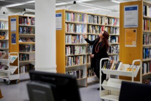 Kirjastoammattilainen silmäilee kirjaston kirjahyllystä sopivaa teosta.