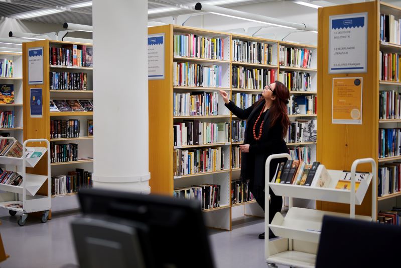Kirjastoammattilainen silmäilee kirjaston kirjahyllystä sopivaa teosta.